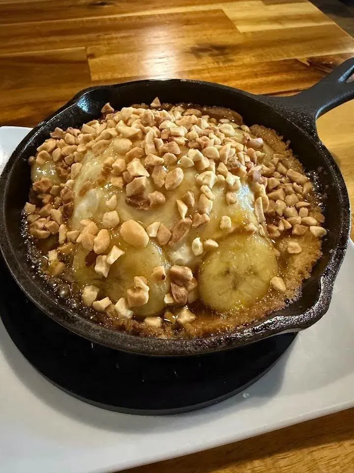 Skillet banana pudding topped with caramelized bananas and chopped peanuts in a cast iron skillet