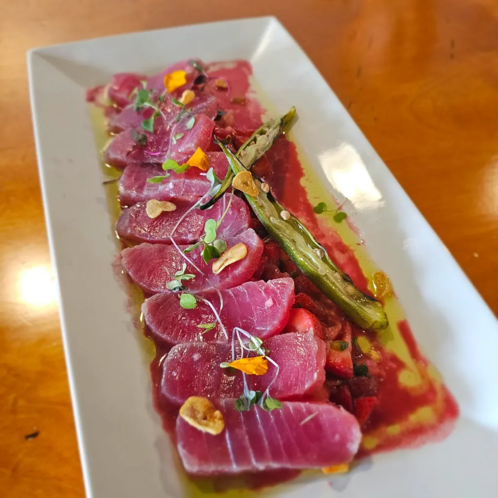 Sliced olive cured blue fin tuna with strawberries, crispy garlic and micro greens