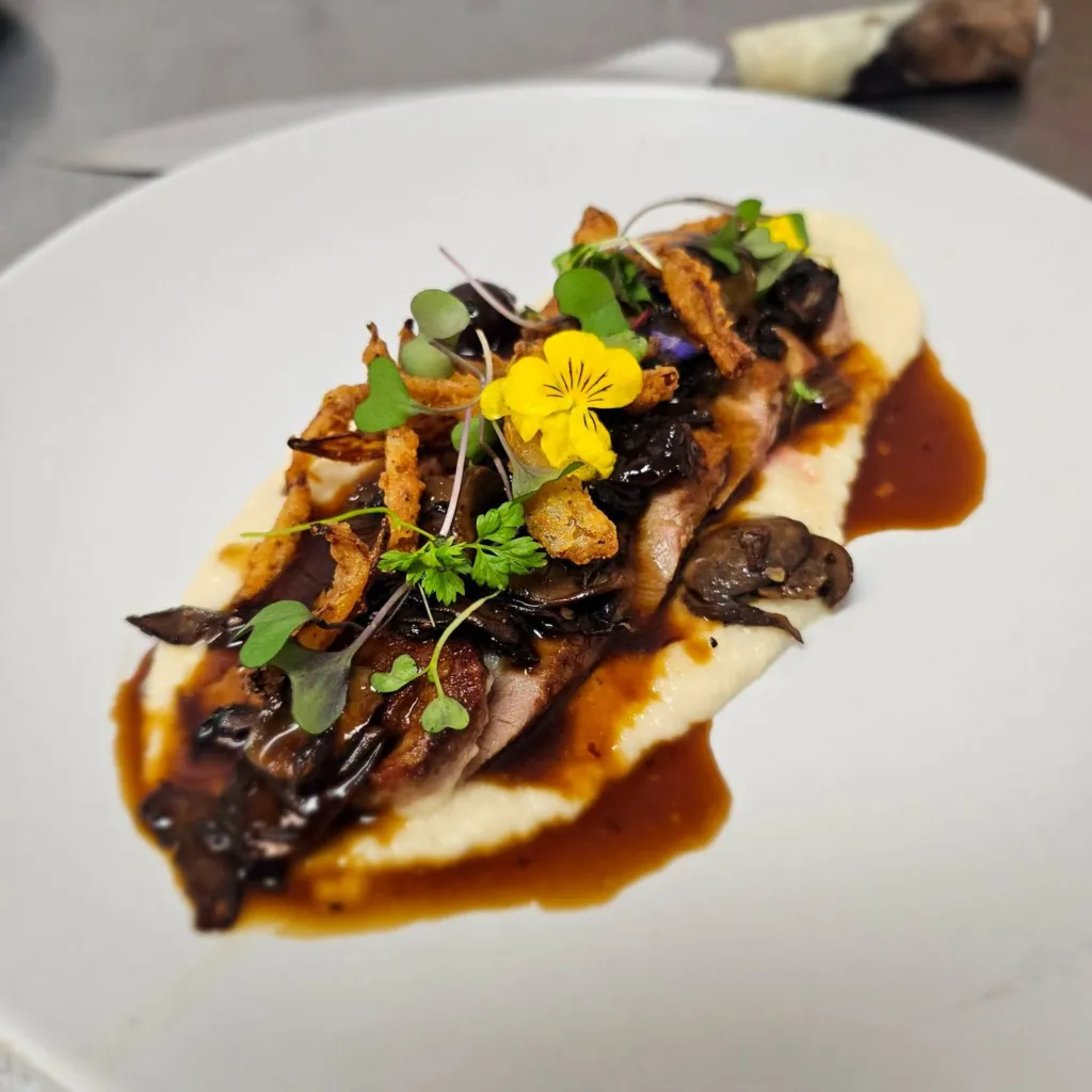 Sliced duck breast over butternut squash risotto with mushrooms, crispy onions and an edible flower