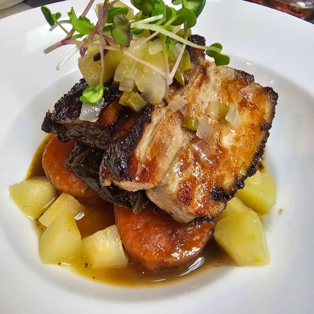 Apple braised pork belly over potatoes and carrots with micro greens